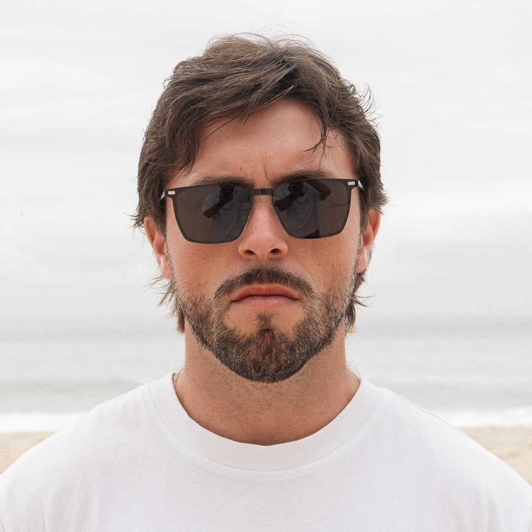 Homem usando óculos Rise 2 em 1 clip-on Fozoco com o clip de sol encaixado, na praia